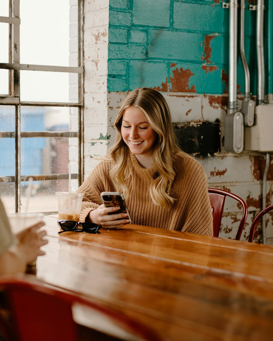 A woman smiling at her phone in a café
