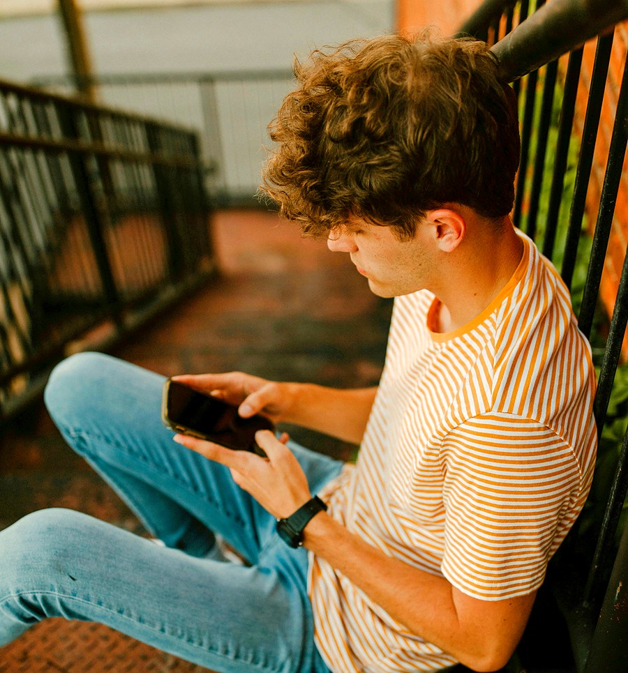 A young man sitting on a bench in warm light, looking at his phone