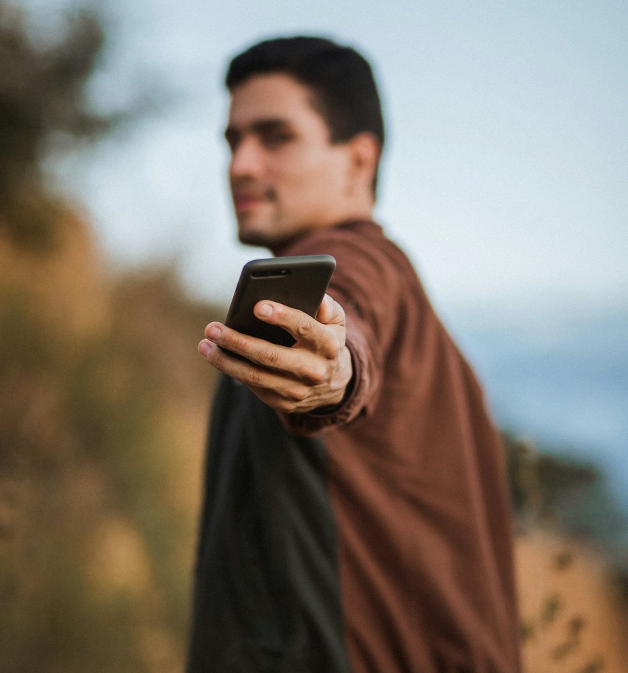 A man outdoors holding out his phone