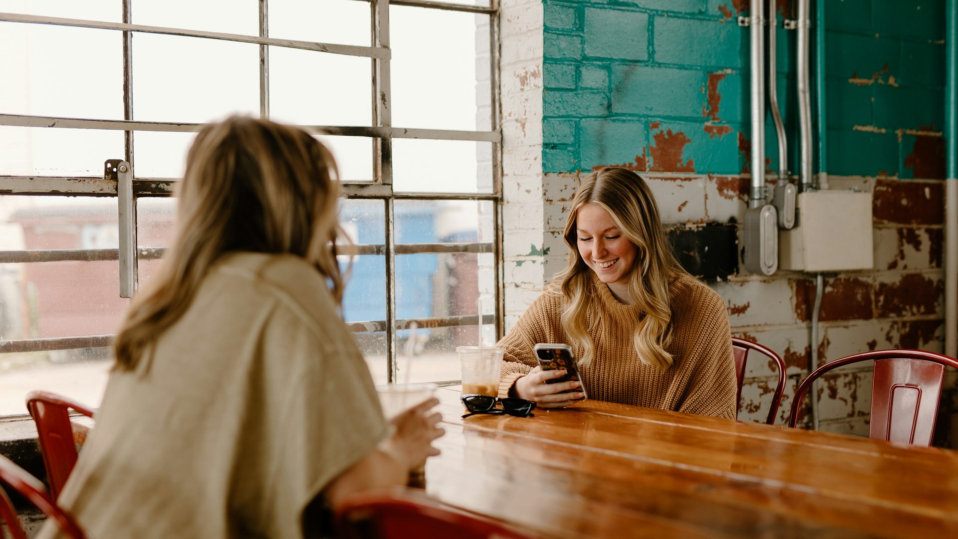 Two friends at a café, one smiling at her phone