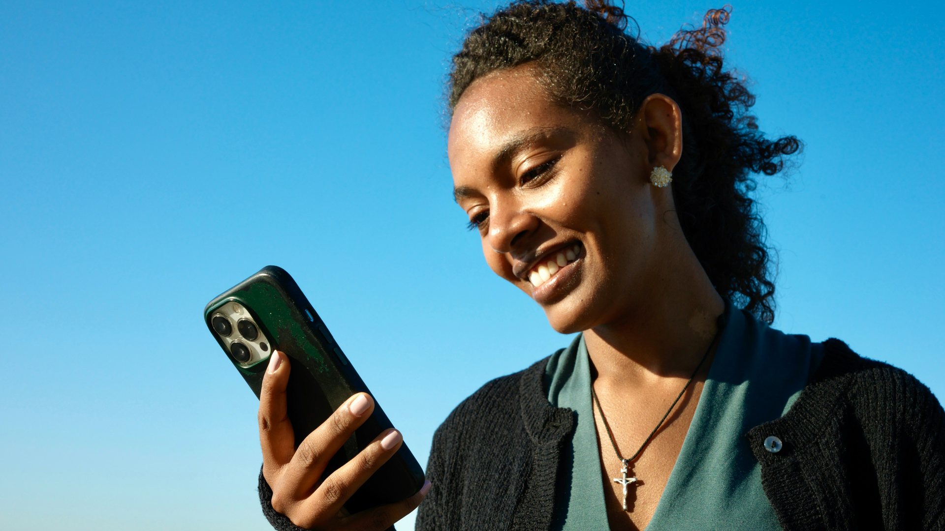 A woman smiling at her iPhone under a clear blue sky