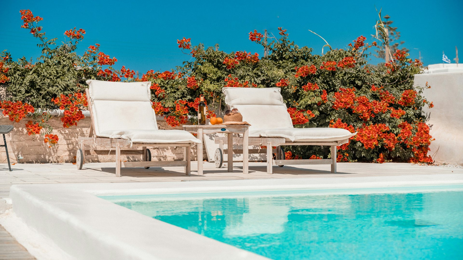 Two sun loungers beside a blue pool and red flowers
