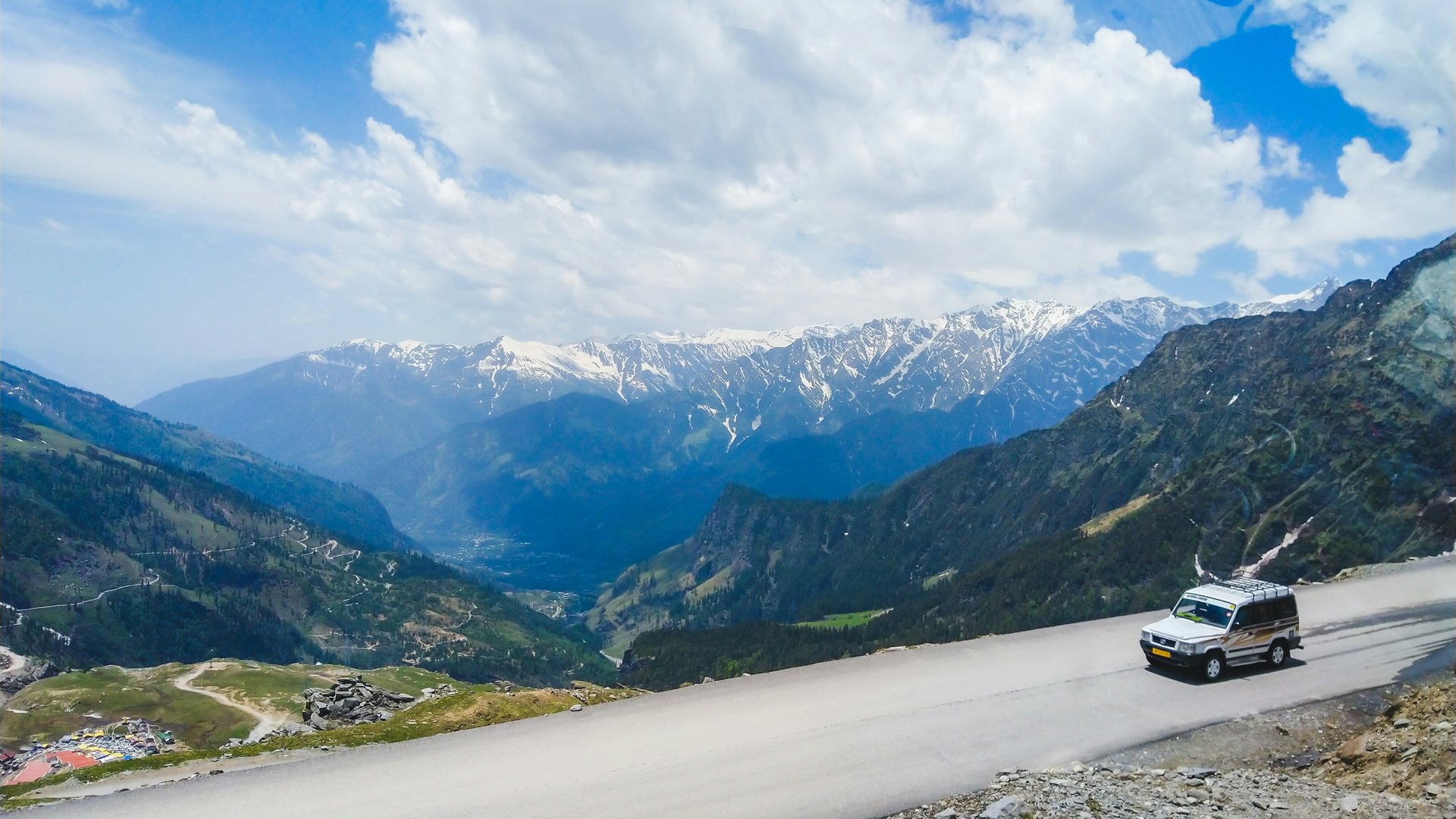 A car on a mountain road under big white clouds