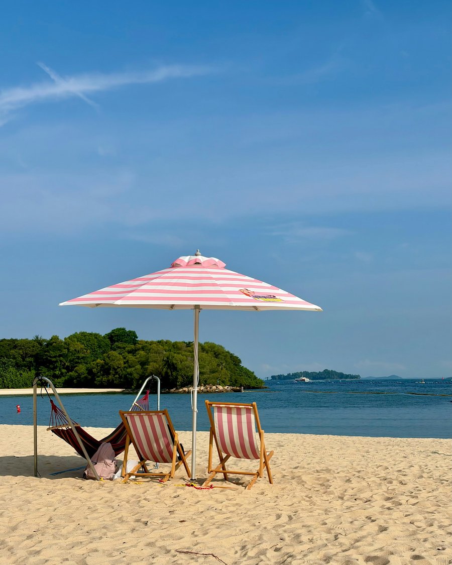 Striped beach chairs under a pink umbrella on a sunny beach