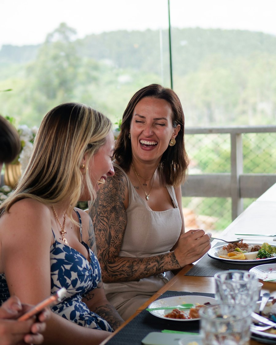 Two friends laughing over lunch at a table with a view