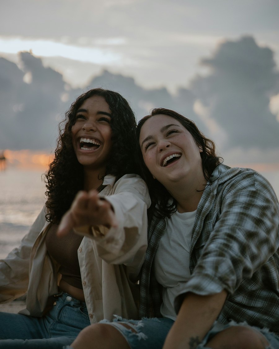 Two friends laughing together on a beach at sunset
