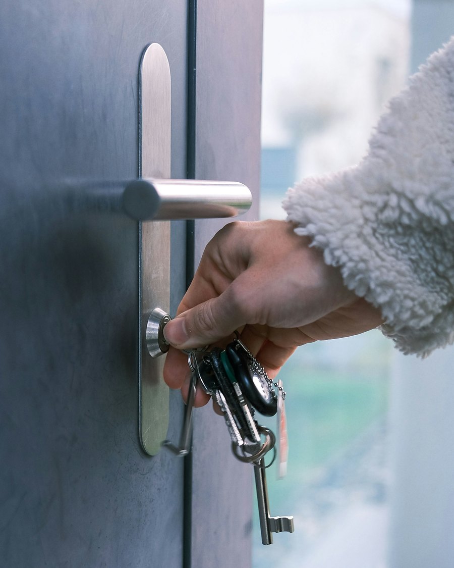 A hand unlocking a front door with a set of keys